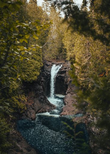 A vertical shot of a waterfall flowing down the stream near rocks and plants