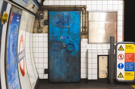 A vibrant blue door in a London Underground station with warning signs and tiled walls, capturing urban infrastructure.