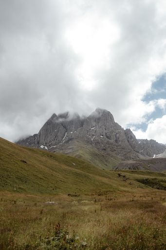 A vertical shot of a rocky mountain and dry field under a cloudy sky