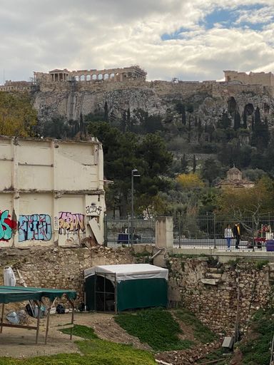 View of the Acropolis in Athens, Greece with ancient ruins and modern graffiti in the foreground under a partly cloudy sky.