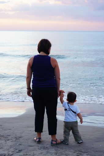 A vertical shot of an adult woman and kid holding hands and standing on the sand near the water at a beach in the evening in Sarbinowo, Poland