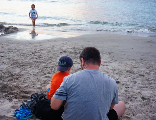 A back view of father and son sitting on a beautiful sandy beach in the evening in Sarbinowo, Poland
