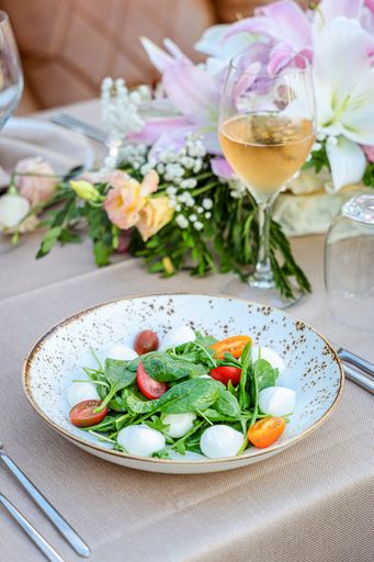 A vertical shot of a salad served in a white bowl and a glass of drink on a decorated table
