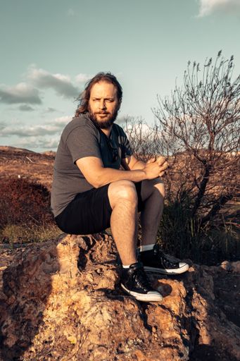 A vertical shot of a serious man sitting on a rock during sunset in Irvine, California, USA