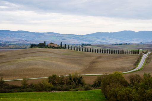 Scenic view of rolling hills and a winding road in the picturesque Tuscan countryside under a cloudy sky.