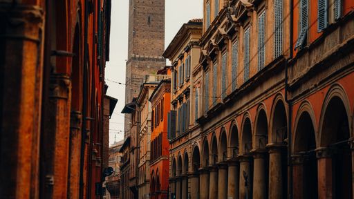 Charming street view of Bologna, Italy, showcasing historic architecture with tall towers and arches under a warm, soft light.