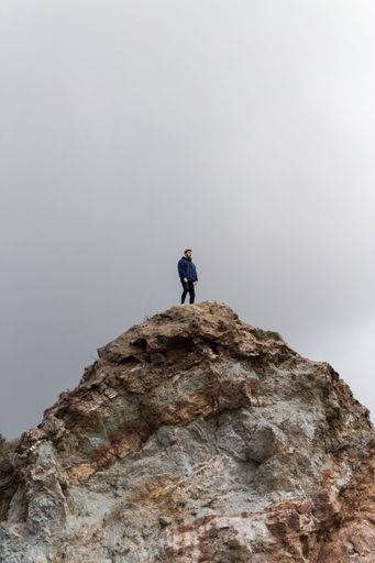 A solitary man stands atop a rocky hill under an overcast sky, symbolizing solitude and adventure.