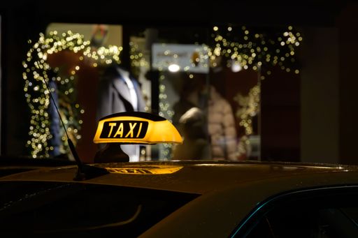 Illuminated taxi sign at night with festive lights in the background, capturing urban nightlife and holiday spirit.