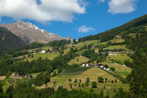 The cloudy sky over the high mountains with coniferous forests, meadows and peaks