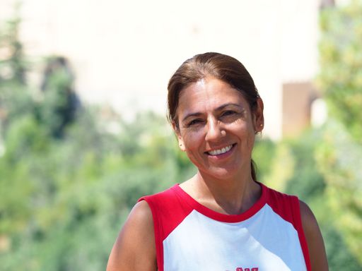A portrait of a smiling Latina woman with her hair up and wearing a casual red and white t-shirt.