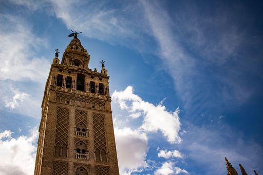 The Giralda tower in Seville, Spain, under a vibrant blue sky with scattered clouds