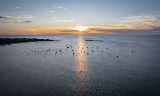A serene sunset over a calm ocean with boats scattered across the water, capturing the tranquil beauty of the seascape.