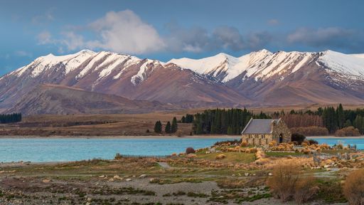 A view of the Church of the Good Shepherd by Lake Tekapo with snow-capped mountains in the background.