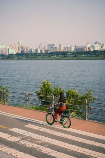A vertical shot of a woman riding a bicycle near a lake