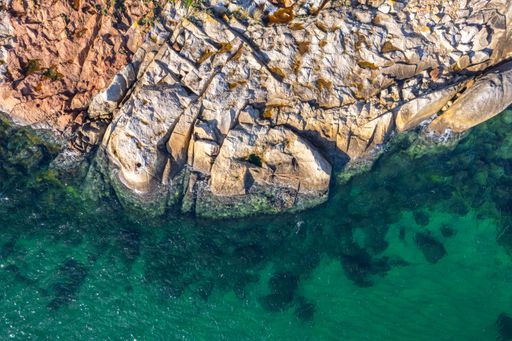 A rocky coastline with turquoise sea water, aerial zenithal view with drone