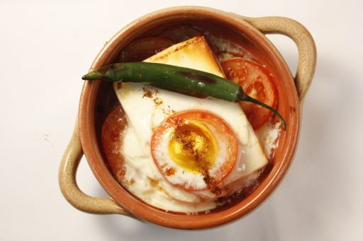 A top view of an omelet and green chili pepper served on a brown plate on a white background