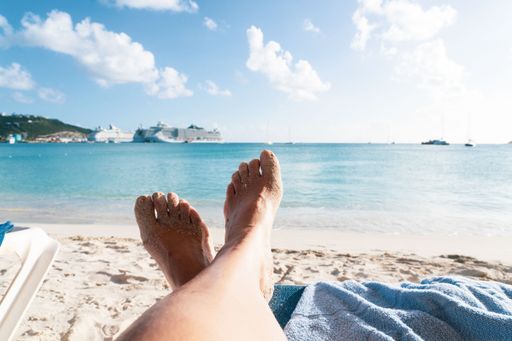 Relaxing on a sandy beach with a view of cruise ships in the distance under a bright blue sky.