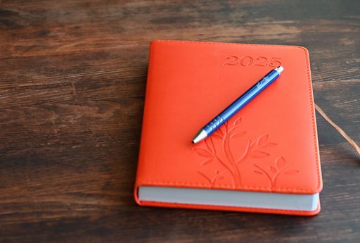 Orange 2025 planner with a blue pen on a wooden table, symbolizing planning and organization.