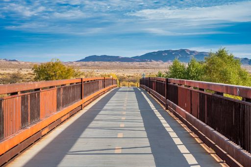 A scenic view of a pedestrian bridge leading to a desert landscape with mountains under a clear blue sky.