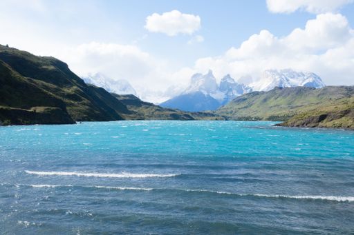 Scenic view of turquoise lake with snow-capped mountains in Torres del Paine National Park, Chile, under a partly cloudy sky.