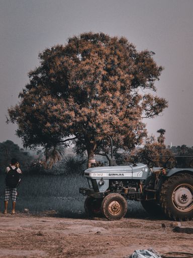 A vertical shot of a tractor and a man next to it photographing the nature of the village in India