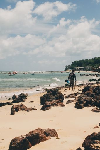 A scenic beach with rocks and a person walking along the shore under a partly cloudy sky.