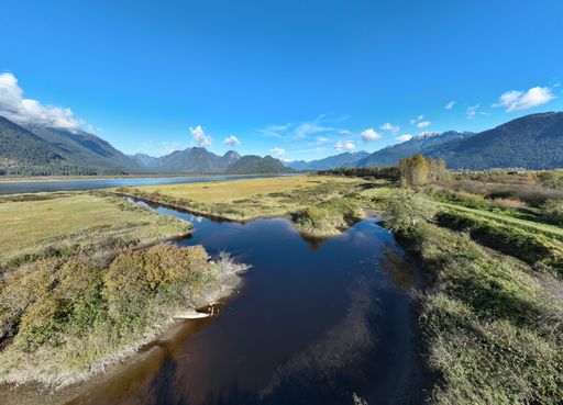 Scenic view of a river winding through a lush valley with mountains in the background under a clear blue sky.