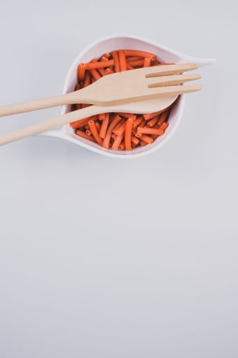 A bowl of dry macaroni pasta with wooden spoon and fork isolated on a white background with free space for text