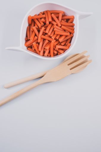 A bowl of dry macaroni pasta with wooden spoon and fork isolated on a white background with free space for text