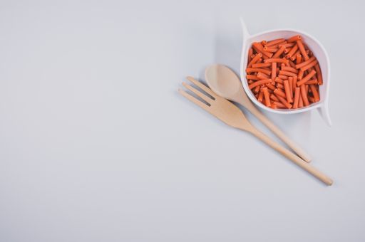A bowl of dry macaroni pasta with wooden spoon and fork isolated on a white background with free space for text