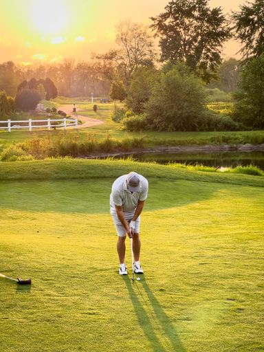 Golfer playing on a lush green course during sunset