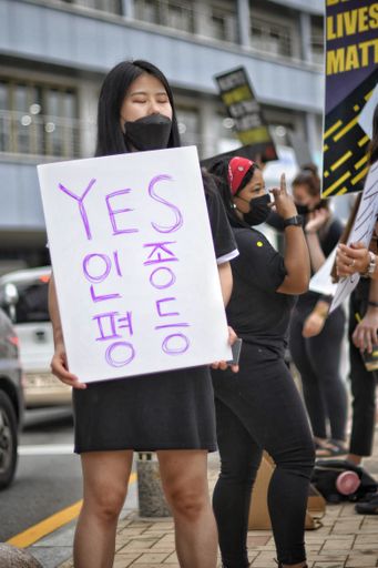 A portrait of an Asian woman holding a poster during the Busan BLM protests in South Korea