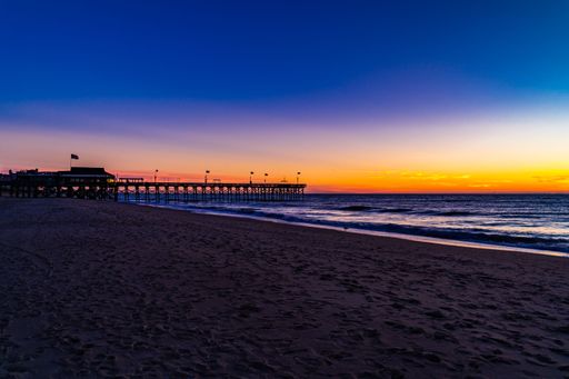 A serene beach sunset with a pier extending into the ocean, vibrant sky colors reflecting on the water.