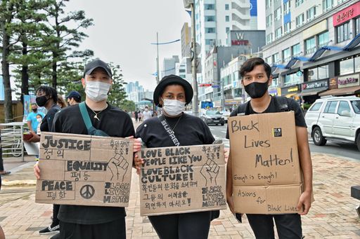 Three young people with a poster protesting during the Busan BLM protests in South Korea