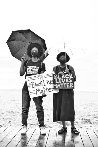 A grayscale shot of two black female protesters holding banners with a sign "Black lives matter"