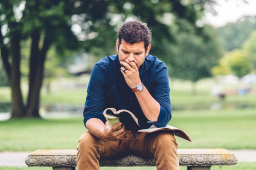A young Caucasian man reading the Bible while sitting on a bench