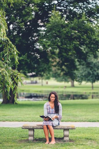 A vertical shot of a Caucasian woman reading a bible at a park