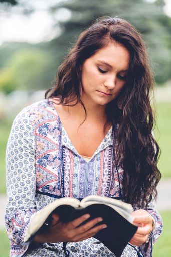 A vertical shot of a Caucasian woman reading a bible at a park