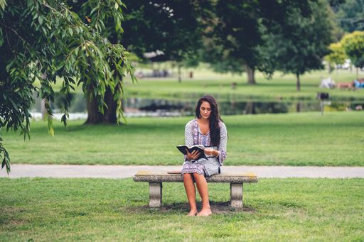 A young Caucasian man reading the Bible while sitting on a bench