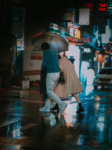 A vertical shot of two people with an umbrella crossing a street during the rain at night in Busan, South Korea