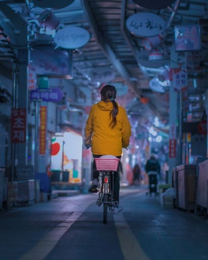A young girl wearing a yellow coat and riding a bicycle through a shopping alley in Busan, South Korea