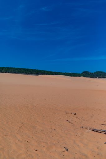 A vertical image of Red Sand Dunes in Mui Ne, Vietnam under a clear blue sky