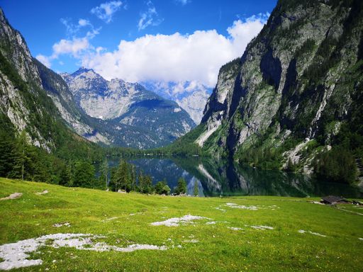 Scenic view of a tranquil alpine lake surrounded by steep mountains and lush greenery under a clear blue sky.