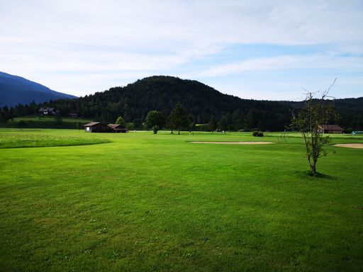 A scenic view of a green golf course with hills and trees in the distance