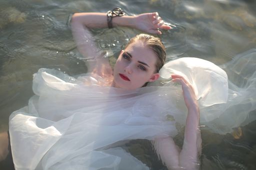 A shot of a young beautiful female in a white dress in the water