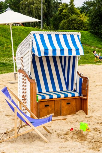 A vertical shot of a wooden striped strandkorb with a deck chair on the sandy bea