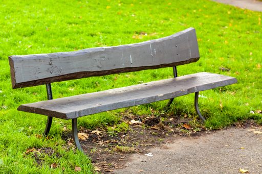 A close-up shot of an old wooden damaged bench in the park on a sunny fall day
