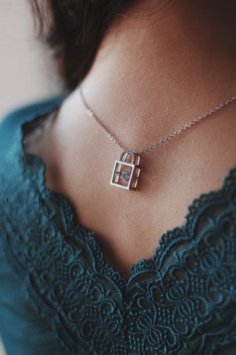 A vertical closeup shot of a female wearing a silver necklace with a beautiful lock pendant