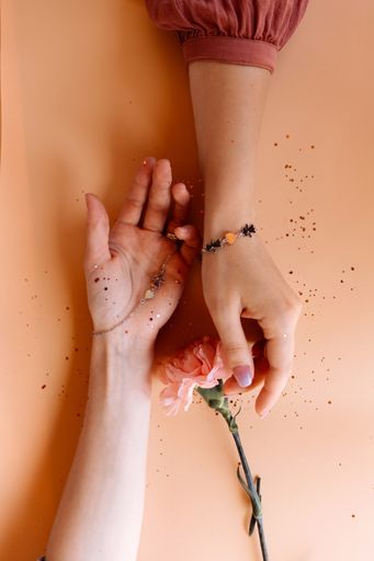 A vertical high angle shot of female hands with beautiful pendant bracelets and a pink flower on a bright orange background with glitters