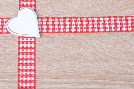 A top view of red ribbons with a heart on a wooden surface with space for text